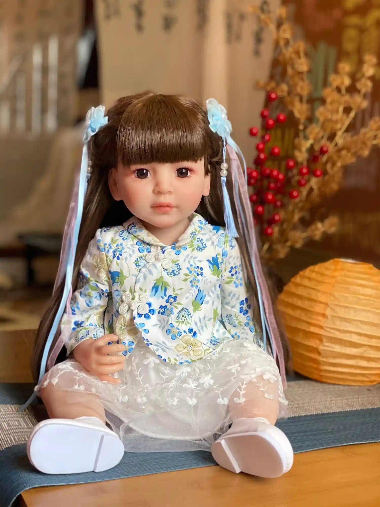 Toddler doll standing, partially hidden by a blue veil, wearing a blue floral dress and white shoes, indoors.