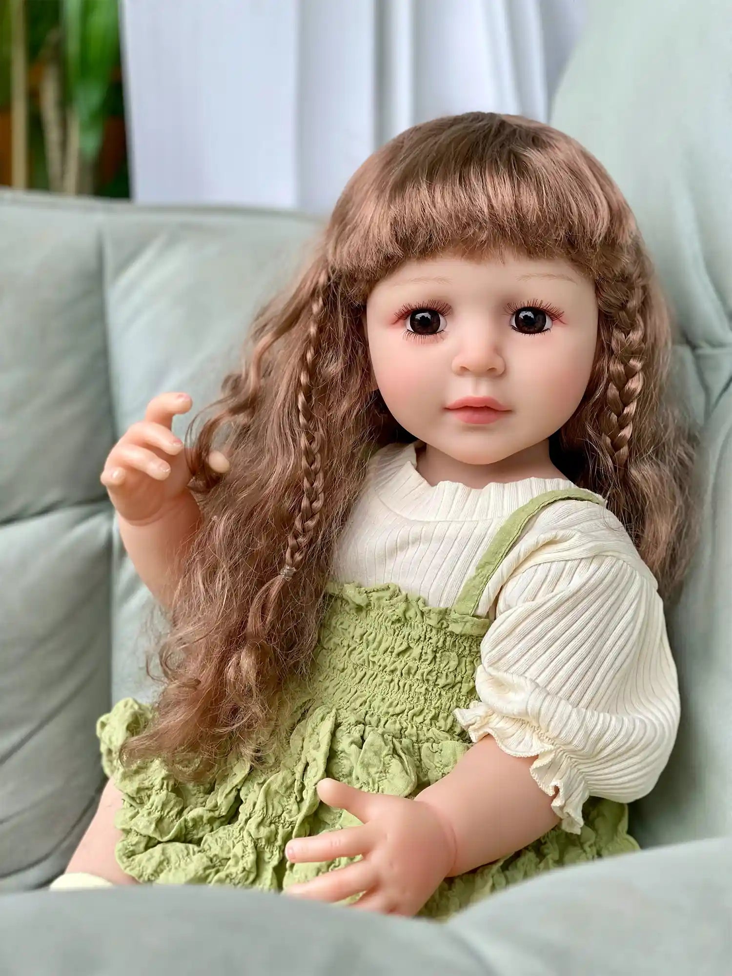 Doll with brown braids and green dress sitting on a grey sofa.