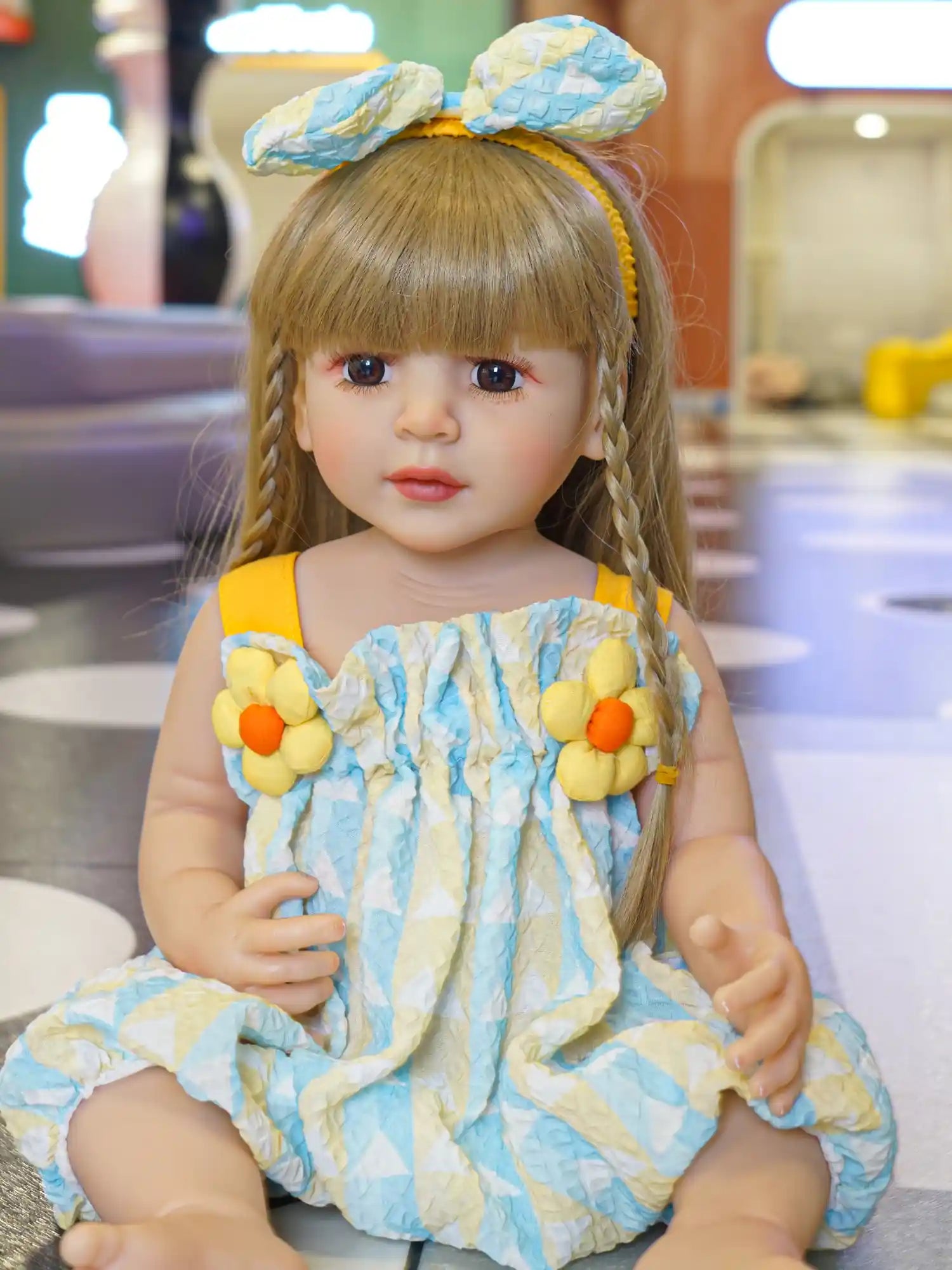 Doll with braided blonde hair in a blue ruffled dress, seated on the floor.