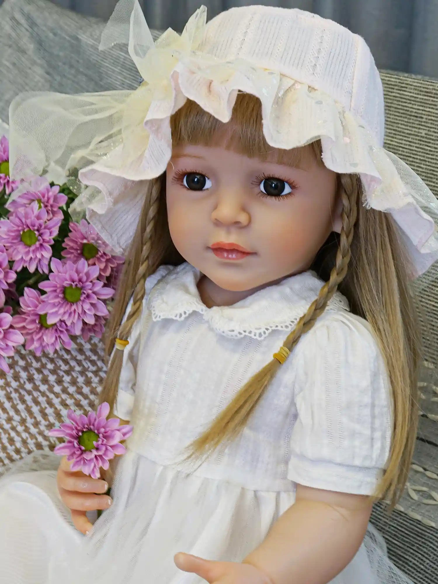 Doll with braided hair and a frilly yellow hat, white dress, on a textured chair.