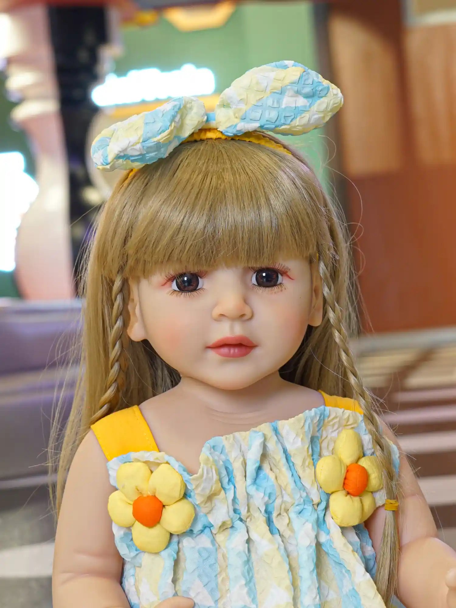 Realistic doll with yellow headband and braids, in a playful dress.