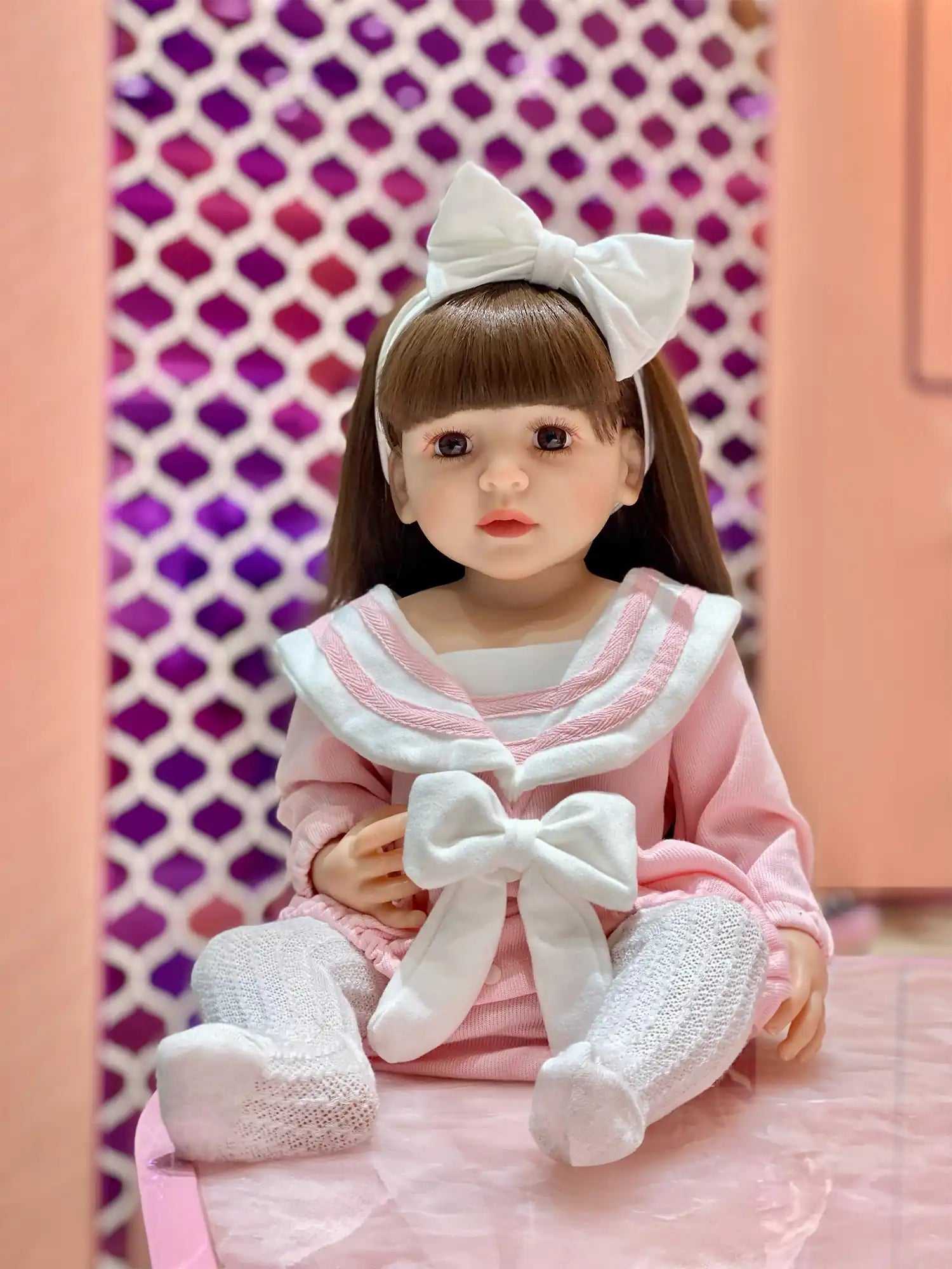 Realistic doll in a pink striped dress and white leggings, seated at a party.