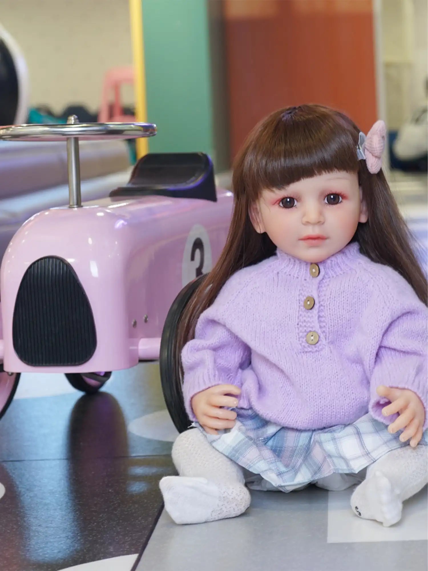Detailed play doll featuring human-like eyes and expression, dressed in a purple top and patterned skirt, resting on the floor.