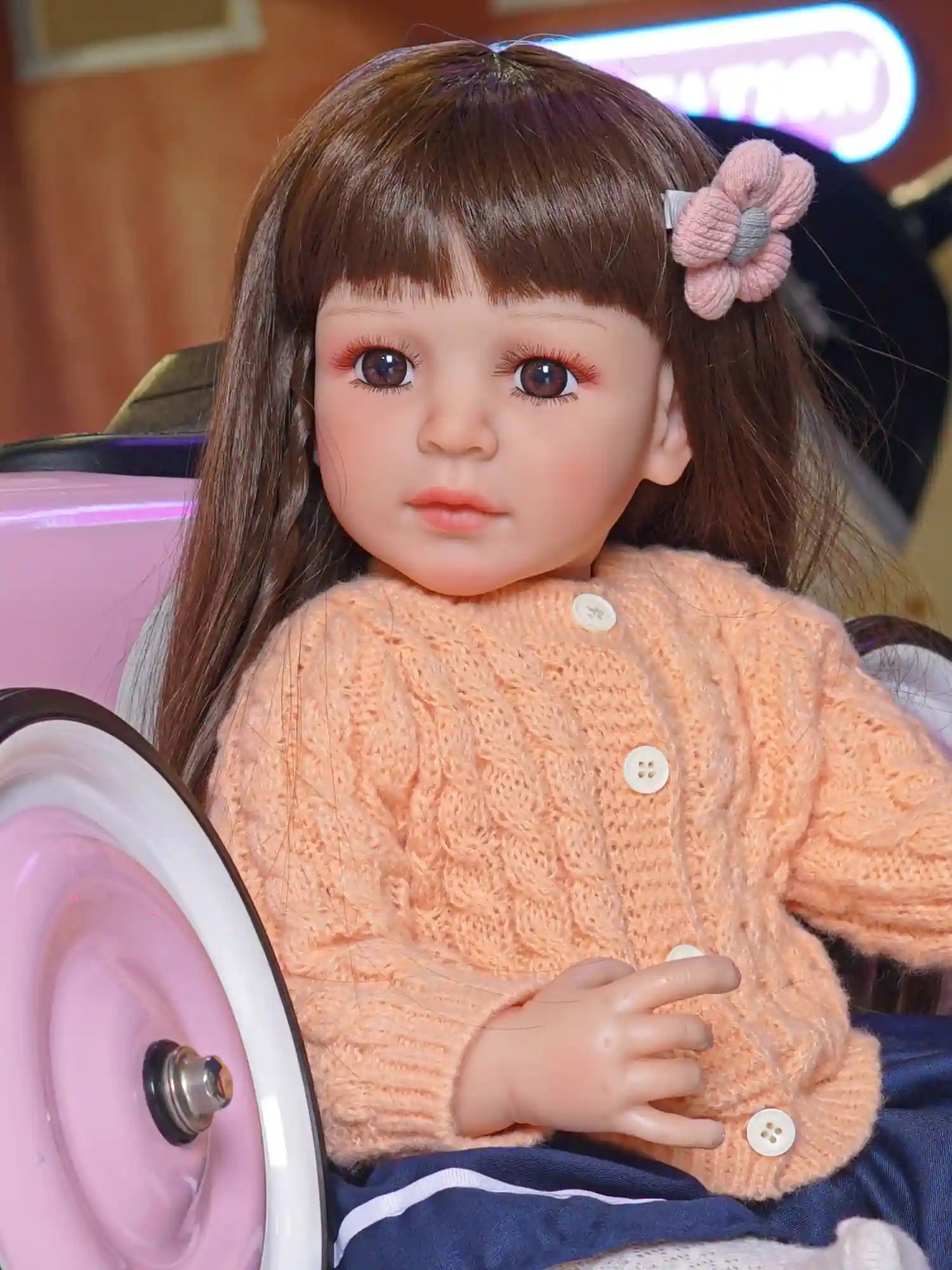Lifelike doll with soft brown hair and expressive eyes, in a cozy knitted sweater and navy pants, in a playroom.