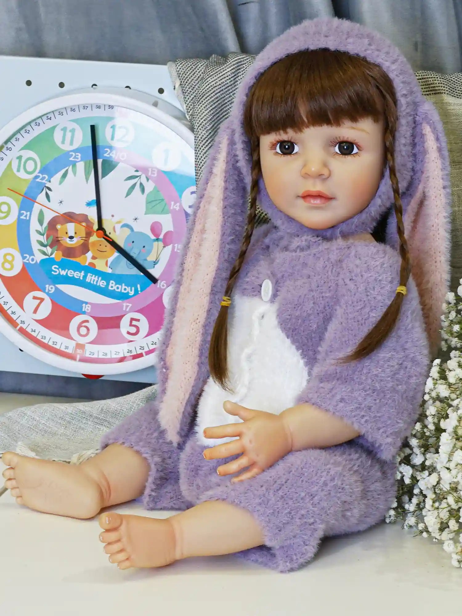 Lifelike reborn doll with brown pigtail braids, capturing a childlike innocence with deep brown eyes, donned in a cozy purple and white bunny outfit.