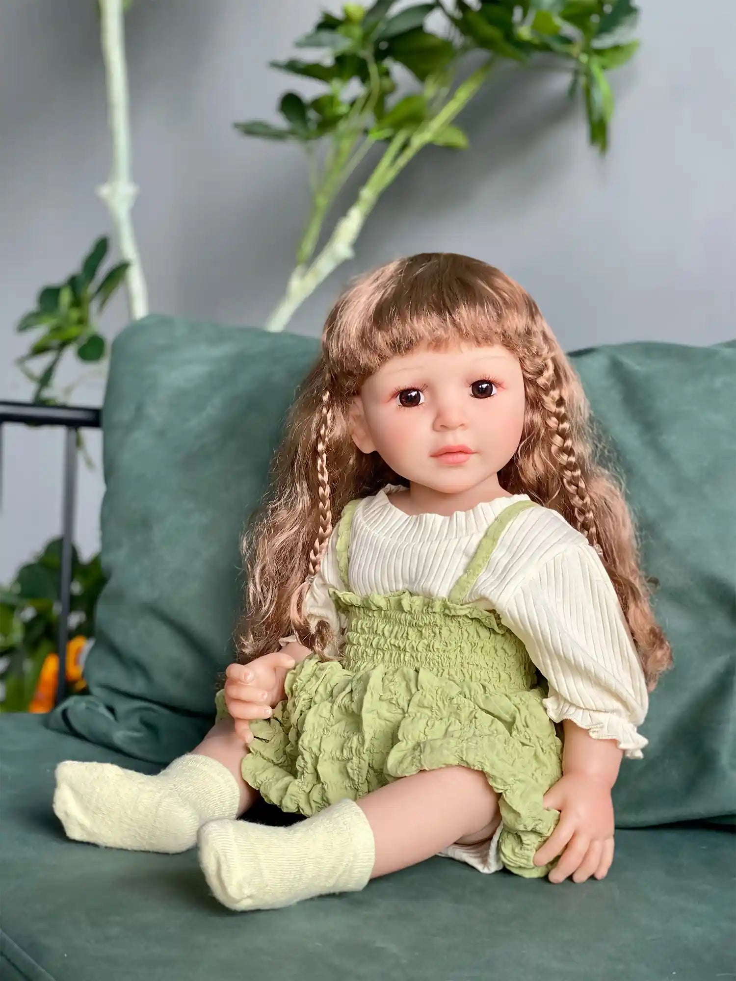 Lifelike doll with braids wearing a green jumper, posing with plants.