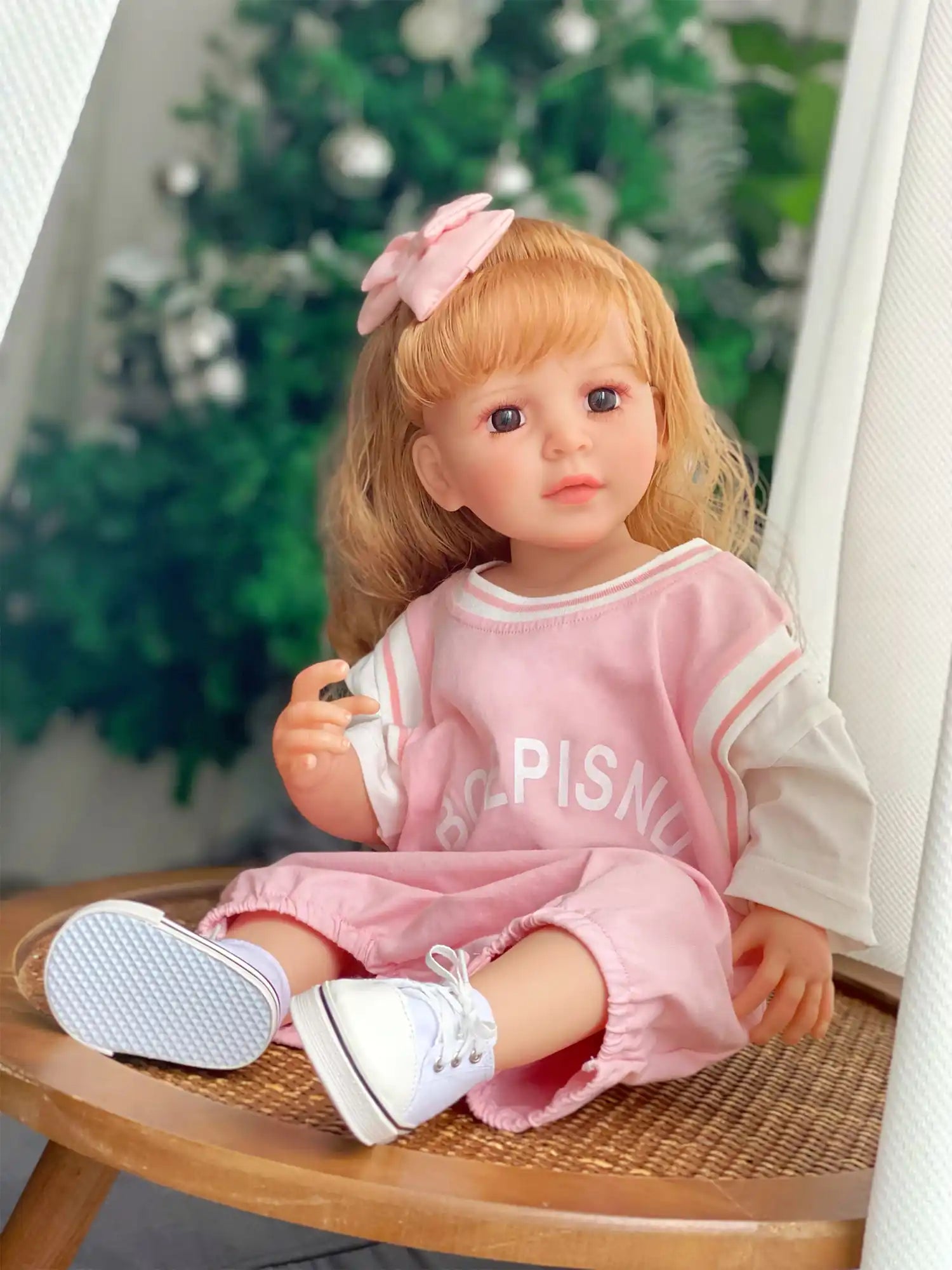 Doll in a relaxed pose, showcasing playful yet fashionable attire, ready for a festive occasion with a decorated tree behind.