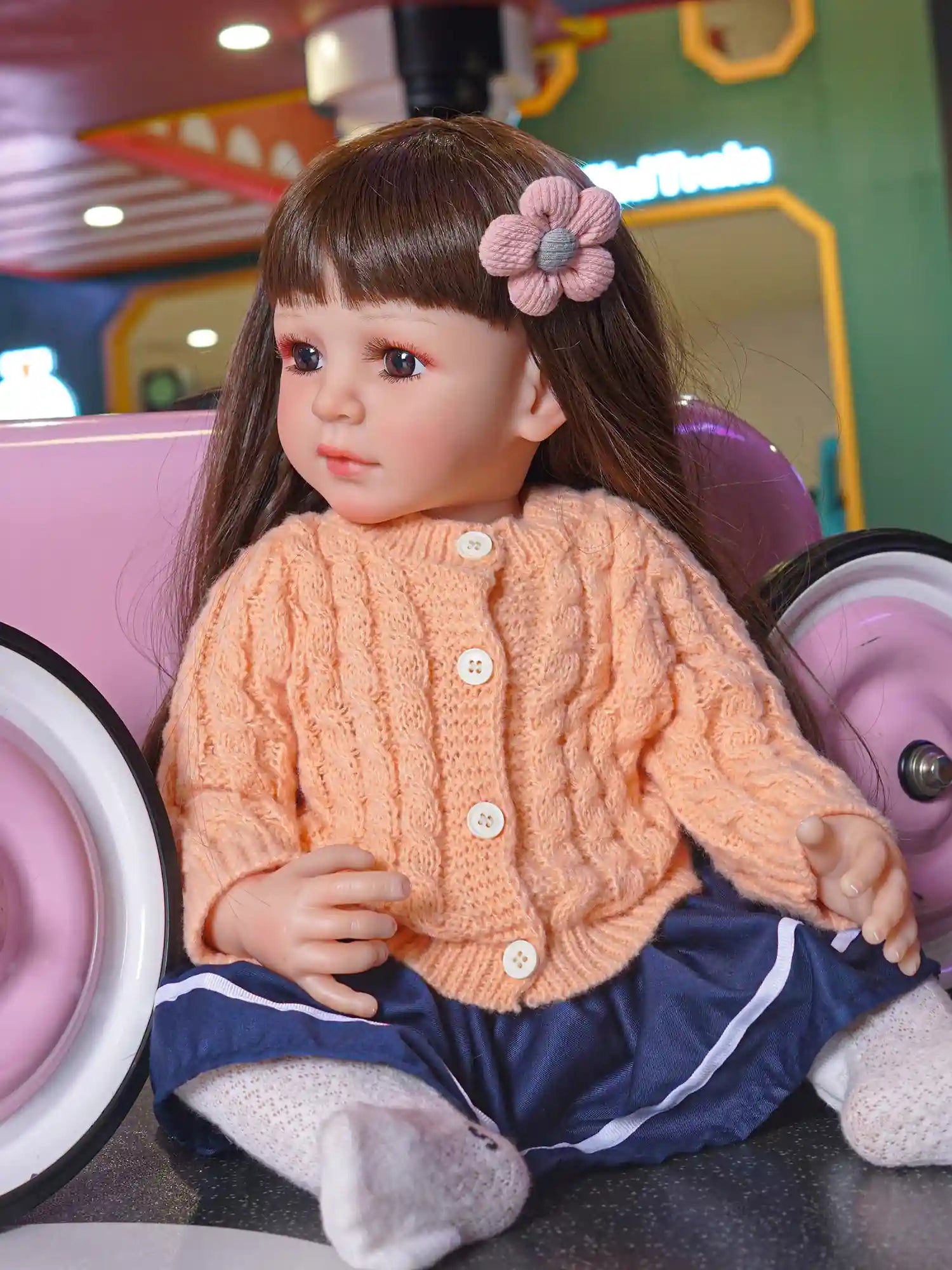Doll dressed in warm autumn colors, with a delicate flower hair clip, gazing thoughtfully beside a child's car.