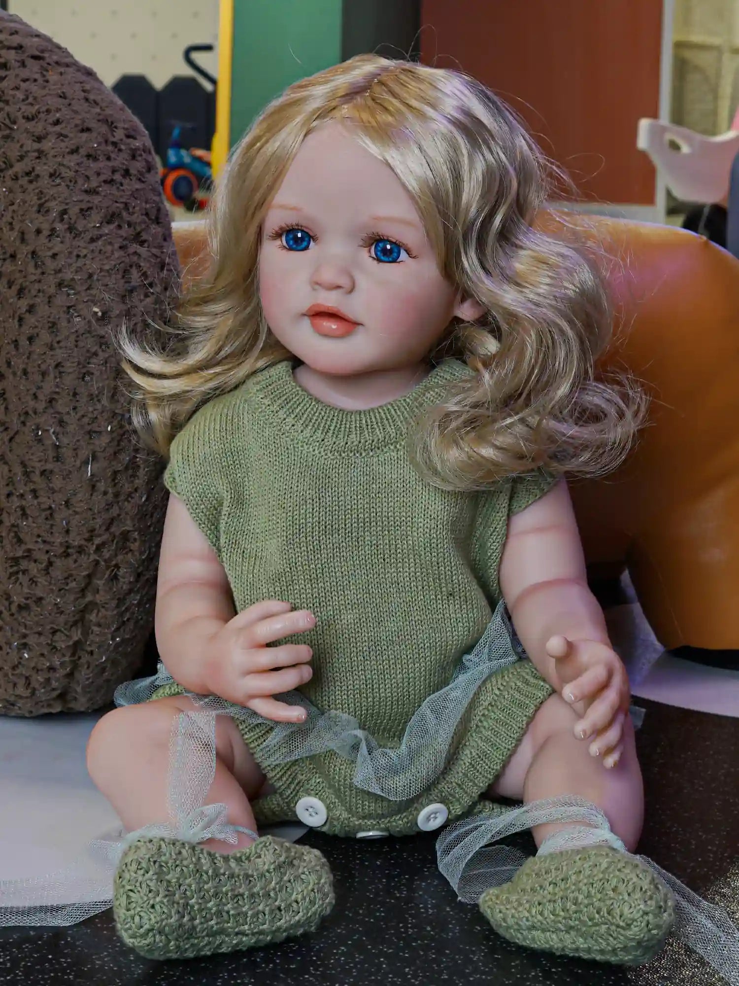Meet our handcrafted reborn doll, a vision of beauty with her golden curls and deep blue eyes, dressed in a soft green knit that whispers of spring.