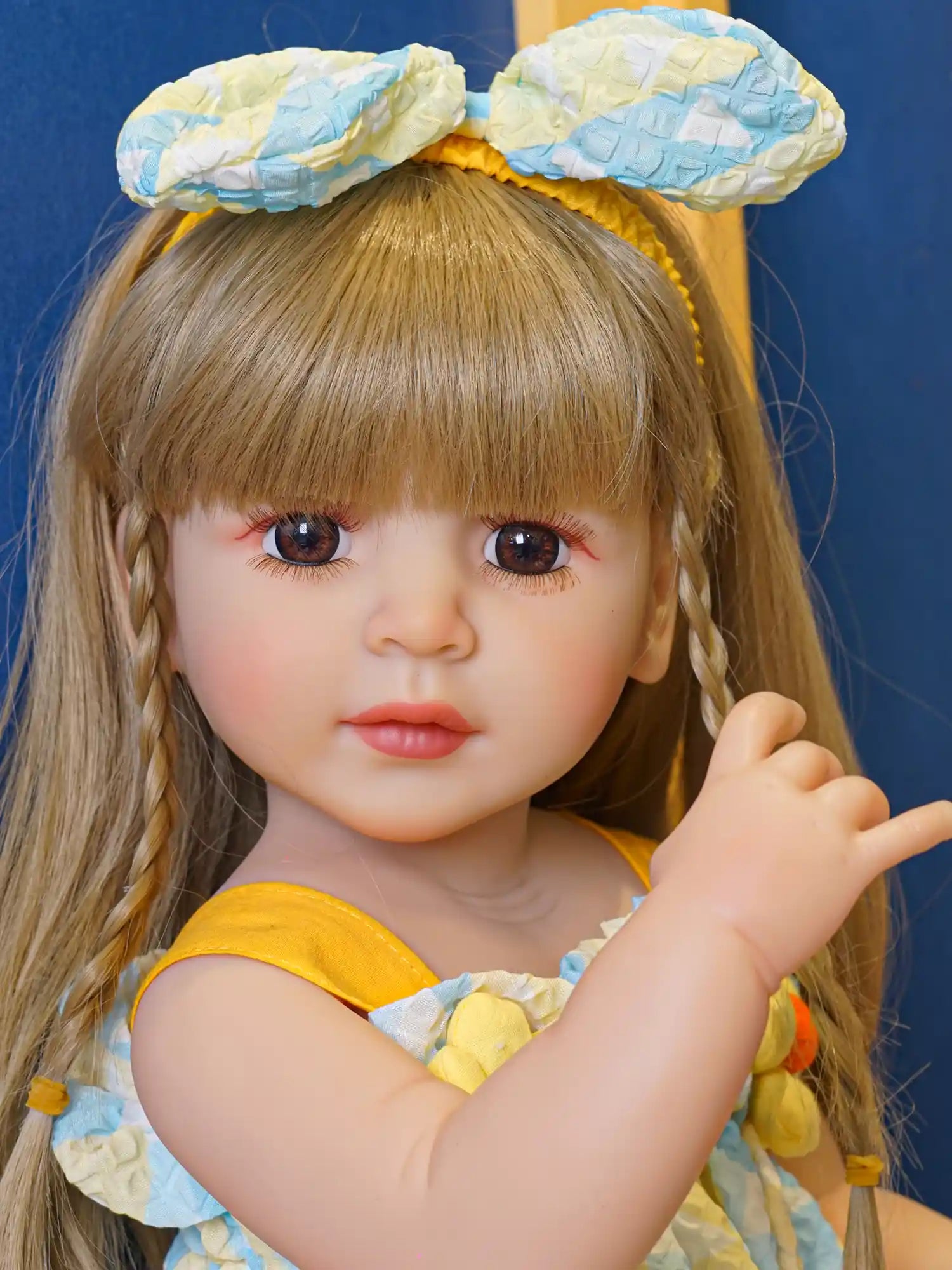 Blonde-haired doll with blue eyes in a pastel blue sundress, sitting comfortably.