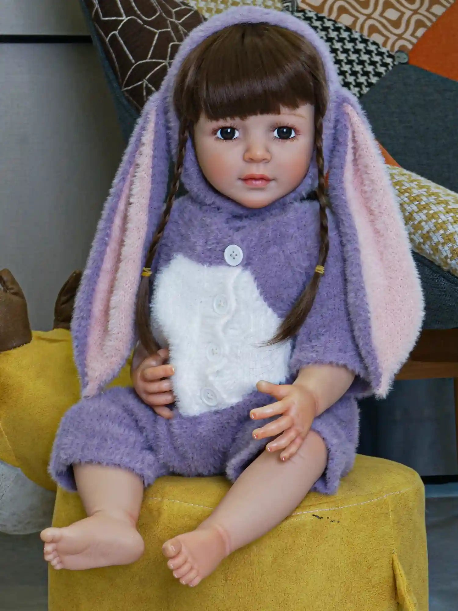Detailed doll with a gentle expression, featuring dark brown braids, sitting comfortably in a playful bunny costume with pastel purple and pink tones.