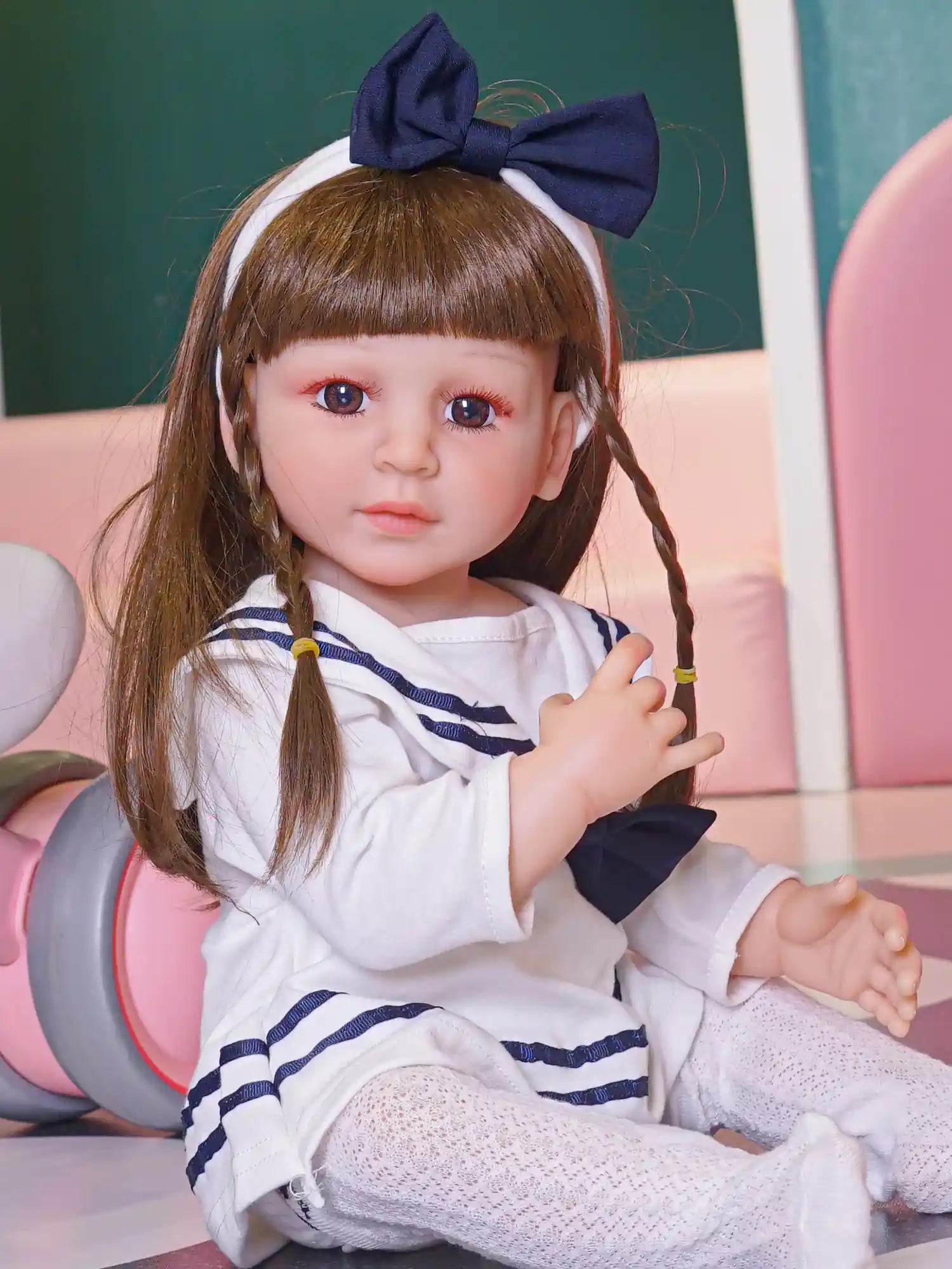 A doll designed to resemble a young child, complete with a lavender sweater and a fabric hair accessory, seated comfortably.