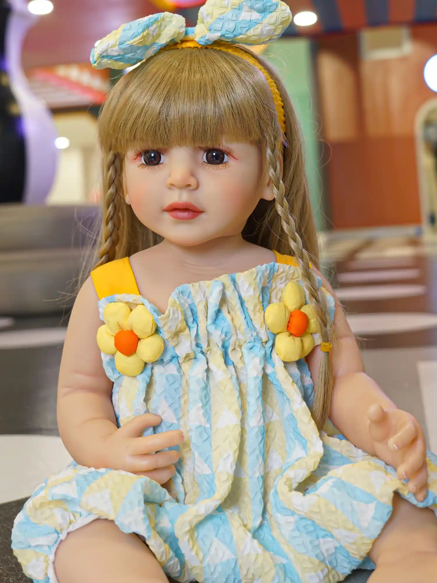A doll in a textured blue dress with yellow details, seated on a gray floor.
