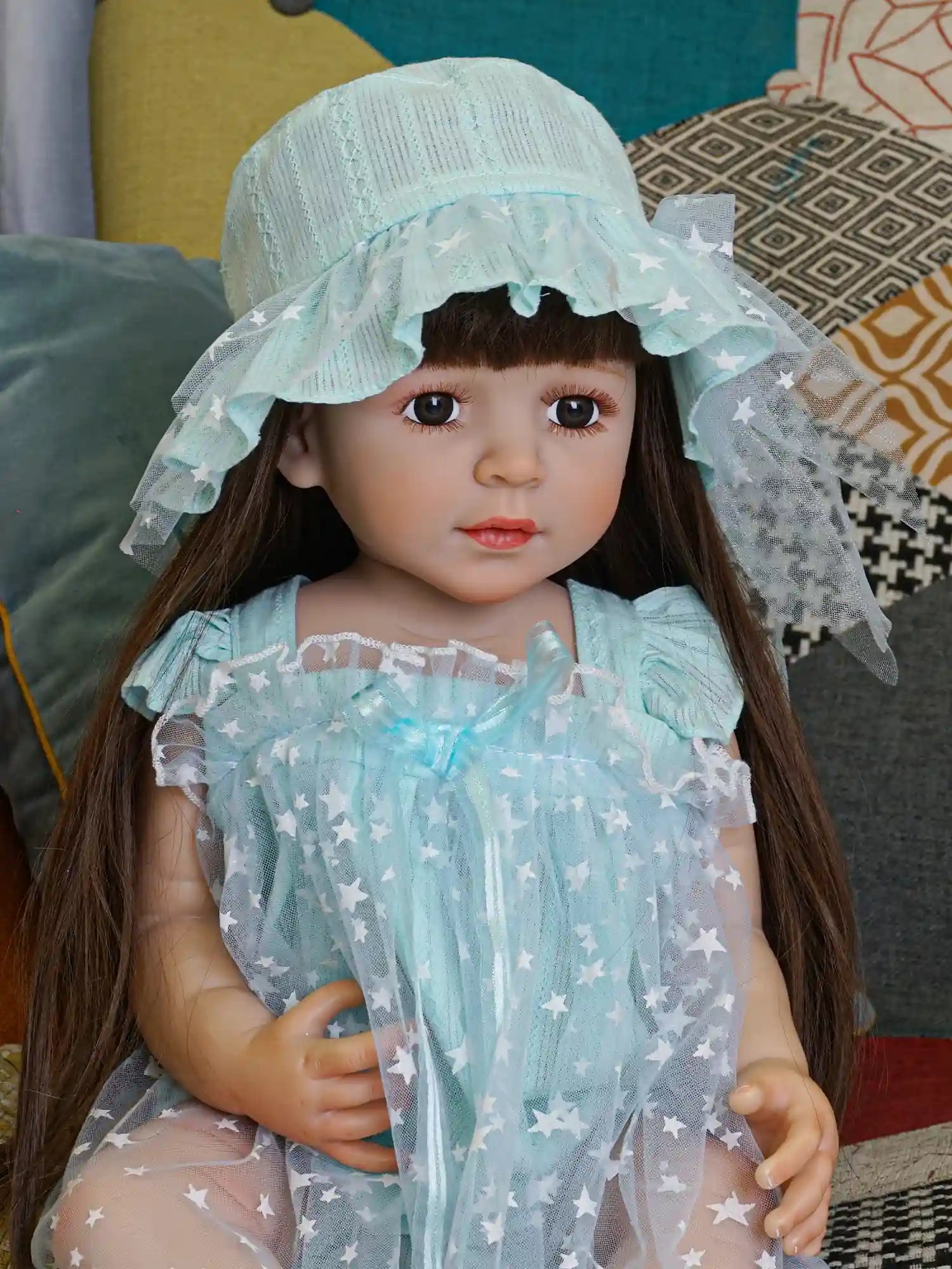 Lifelike doll in a whimsical aqua dress with a frilly bonnet, on a retro chair.