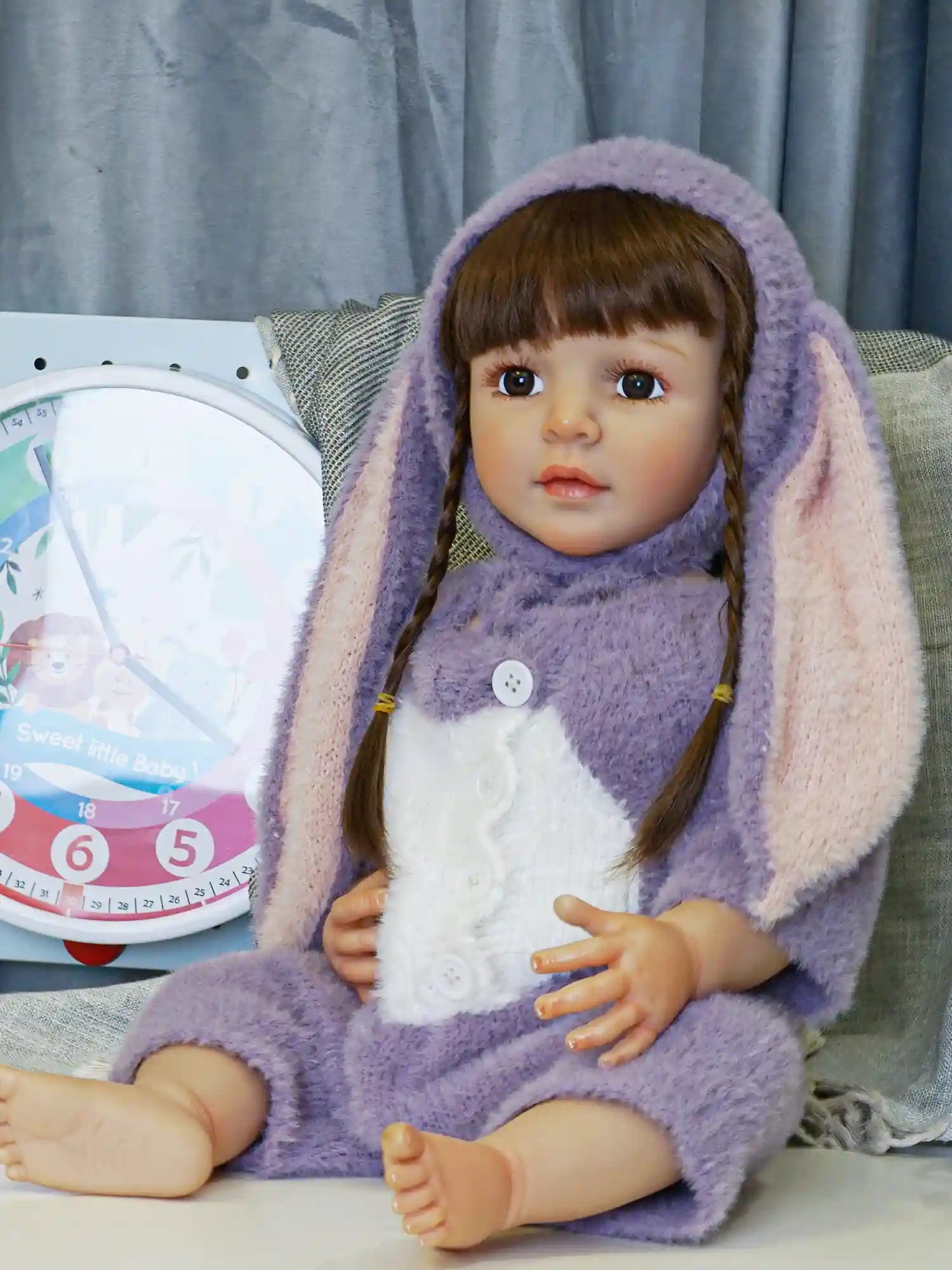 Artisan doll resembling a seated child, with glossy brown hair and curious eyes, outfitted in a whimsical bunny costume with a hood and a white tuft.