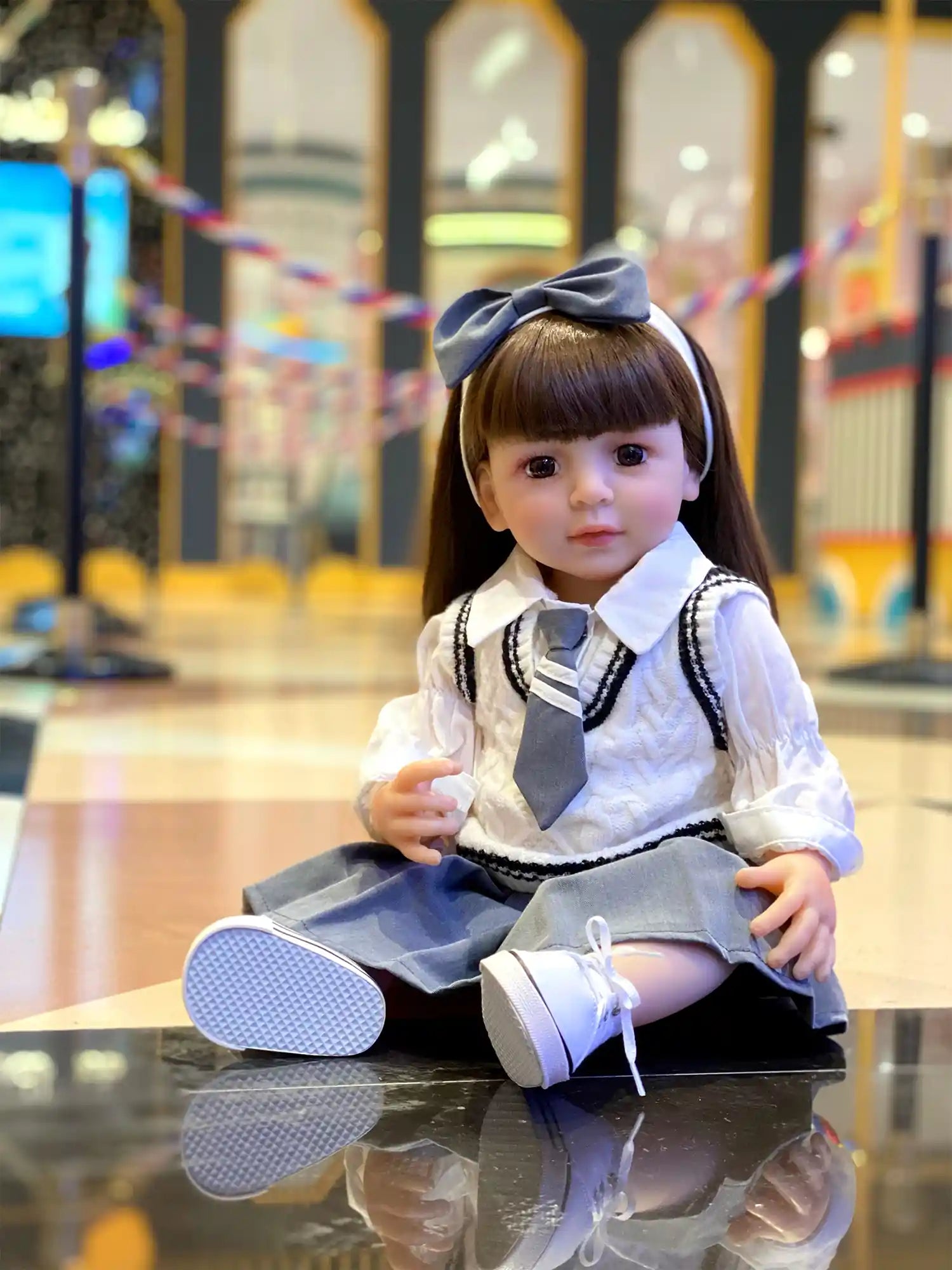 Artisan-crafted doll capturing a schoolgirl’s look, featuring glossy brown hair with bangs and a large grey bow, sitting against a playful, colorful background.