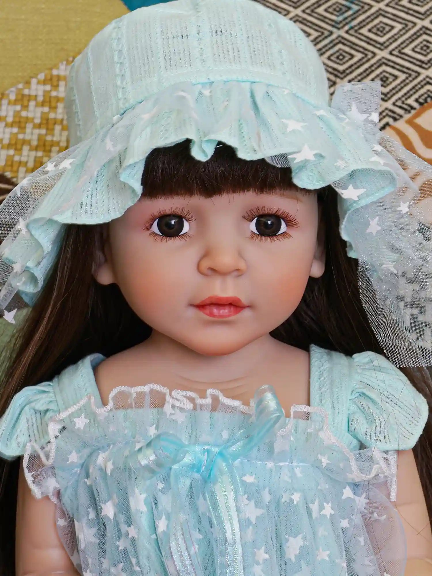 Realistic reborn doll with brown hair, in a starry aqua dress and matching leggings.