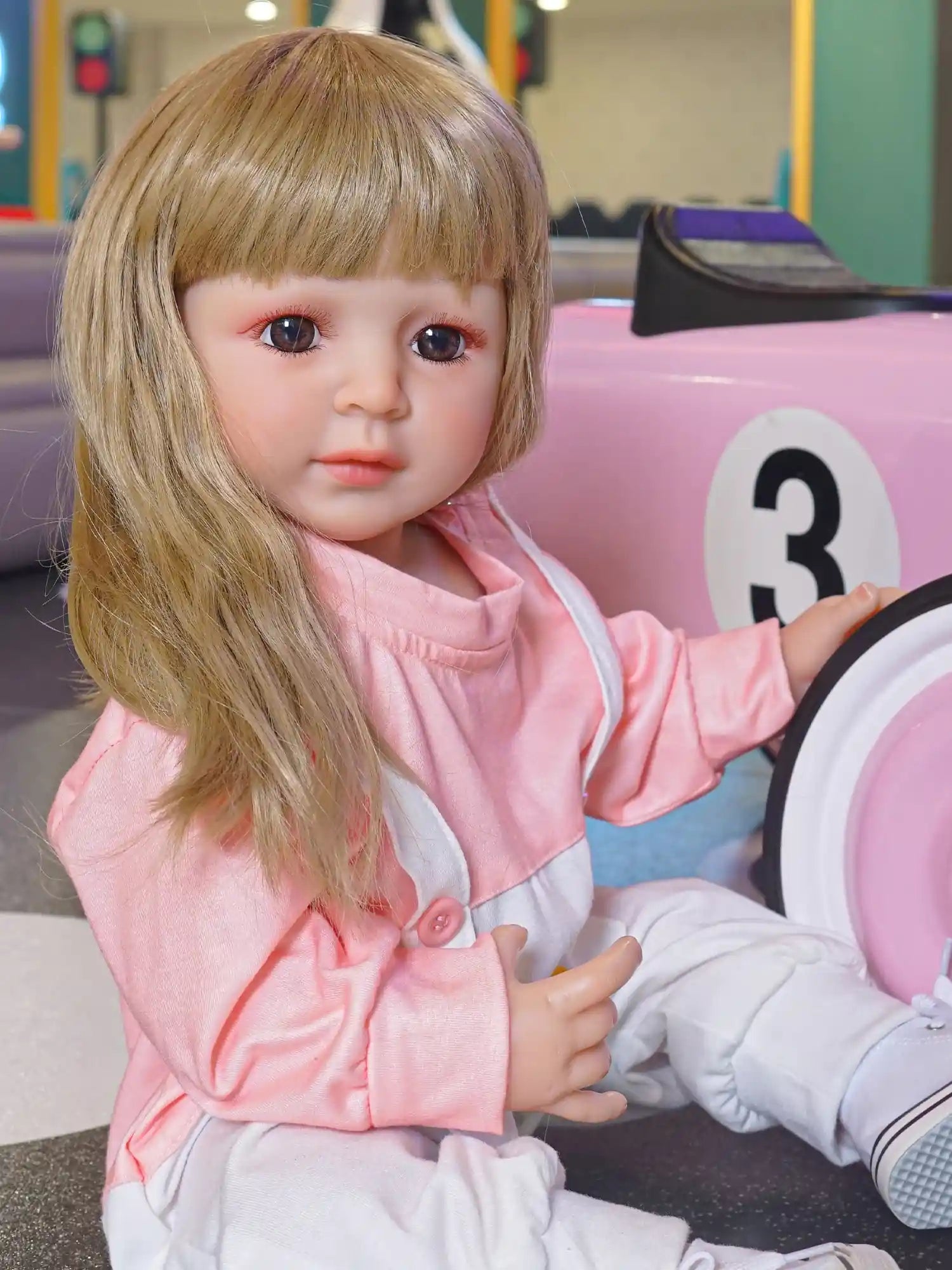Toddler doll capturing a candid moment of playtime, in comfortable attire, with a pink toy vehicle to her side.