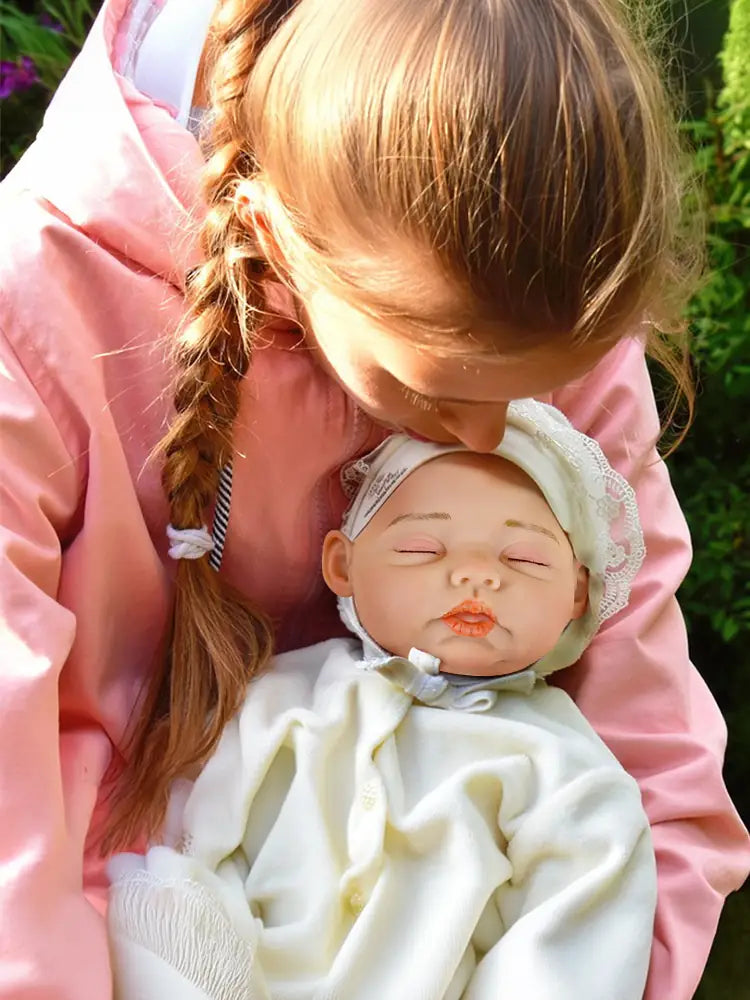 A little girl holds a reborn baby doll in her arms and kisses its forehead