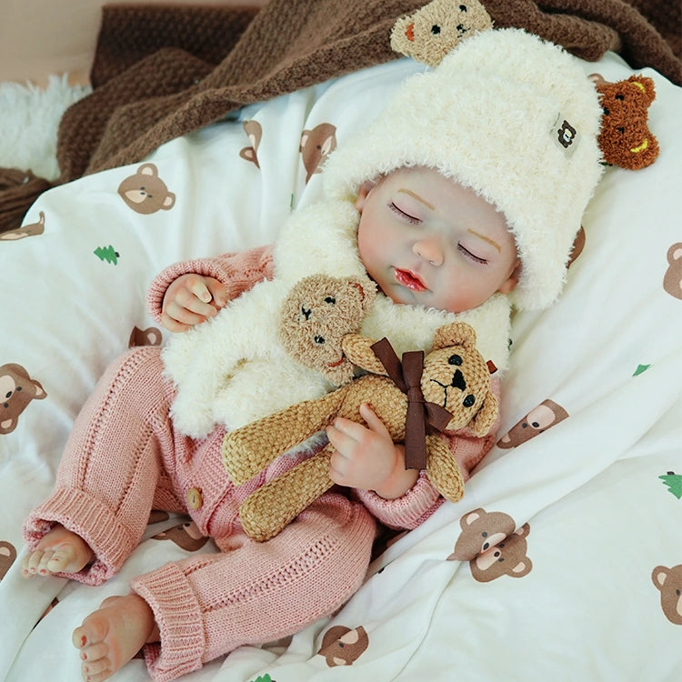 Reborn baby doll lying on a soft bed, cuddling a toy bear, in a serene sleeping position.