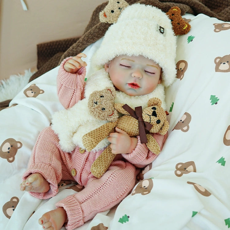 Reborn baby doll in a white sheep hat, peacefully asleep, holding two stuffed bears.