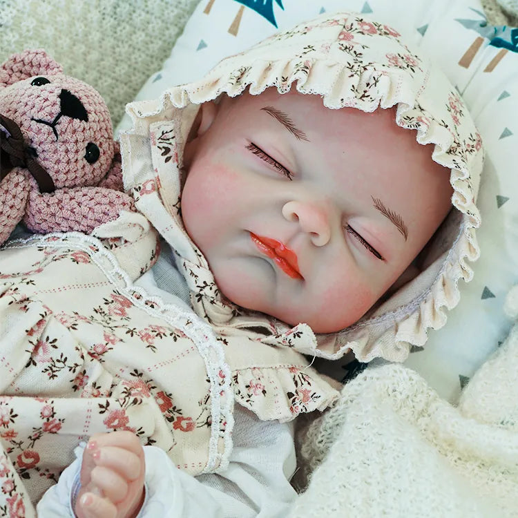  Close-up of the reborn baby doll's peaceful face, wearing a floral bonnet and holding a soft teddy bear, lying comfortably on a blanket.