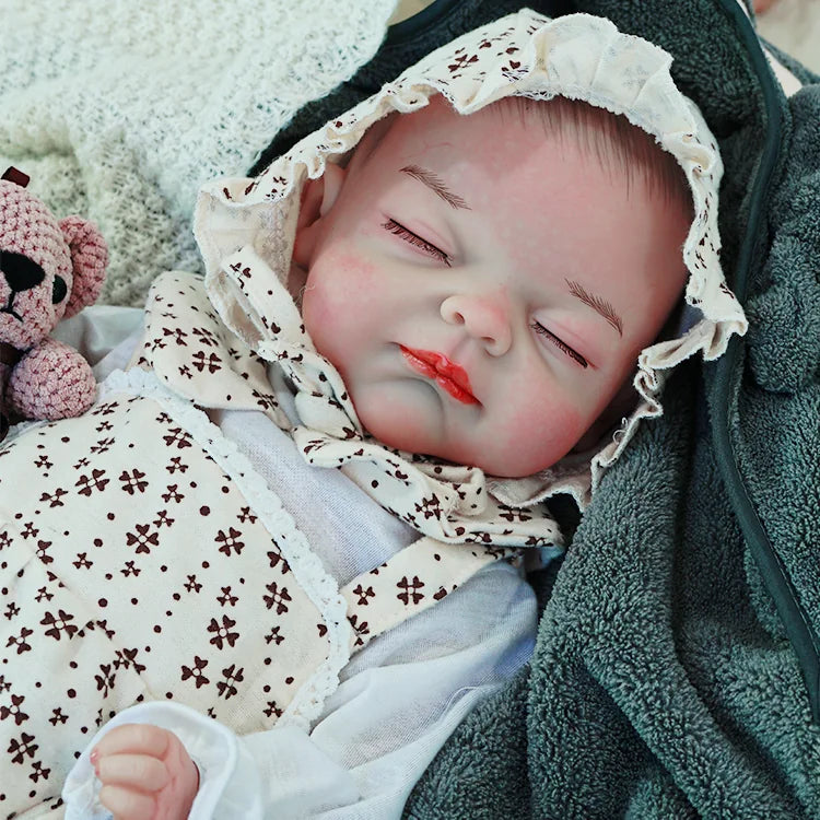 The reborn baby doll resting peacefully, dressed in a floral outfit and bonnet, cuddling with a soft teddy bear.