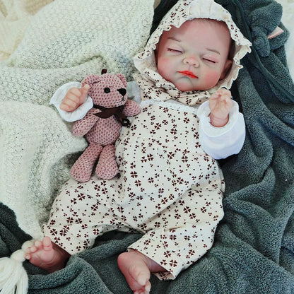 The reborn baby doll sleeping soundly, dressed in a floral onesie with a bonnet, holding a knitted teddy bear while lying on a blanket.