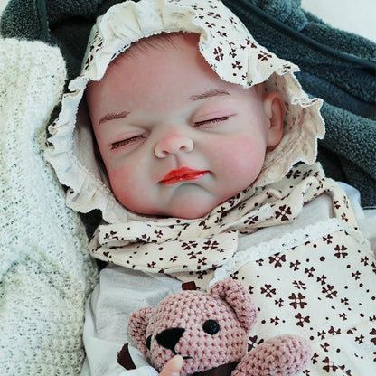 The reborn baby doll peacefully asleep, dressed in a floral onesie and bonnet, holding a knitted teddy bear.