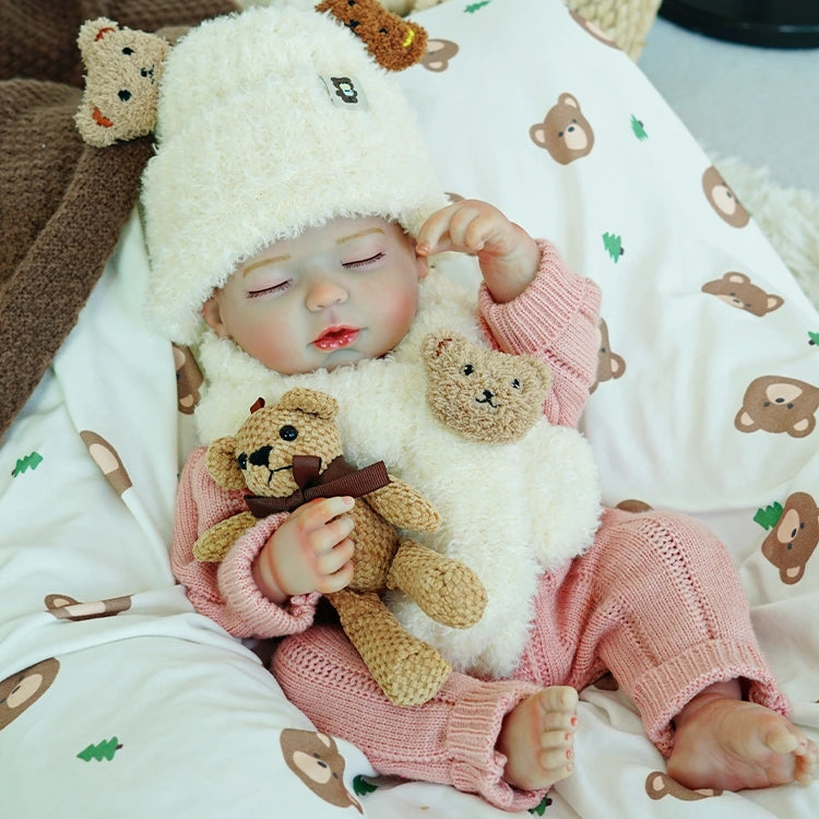 Reborn baby doll in a pink outfit, quietly holding two stuffed bears in a cozy sleeping pose.