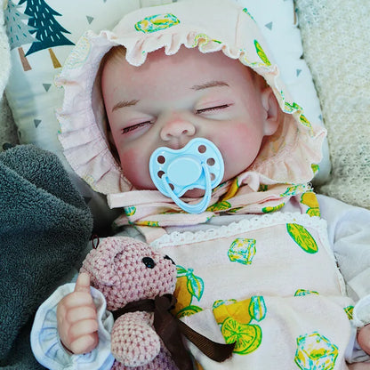 A reborn baby doll with a pacifier, dressed in a lemon-printed outfit, lying on a dark blanket, holding a pink teddy bear.