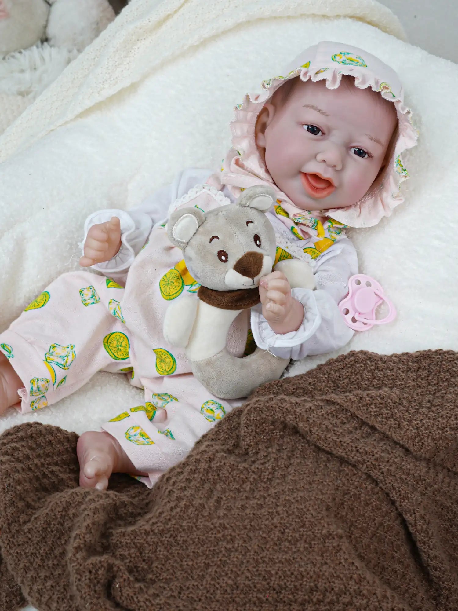 A cute reborn baby doll lying on the sofa holding a teddy bear doll