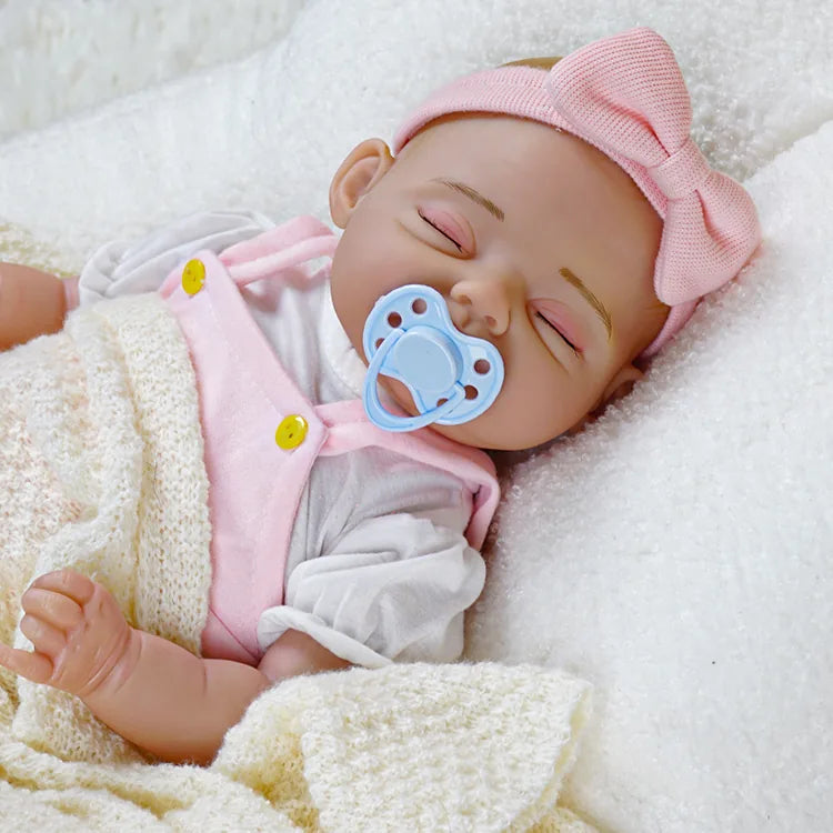 Lifelike newborn doll with a pink bow headband and a blue pacifier resting beside her, wearing pink overalls, depicted in a serene sleeping pose.
