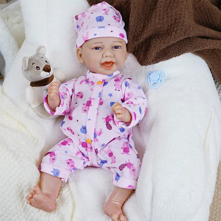 Reborn baby doll in a chef's hat and pink pajamas, holding a pacifier, with a toy bear beside it, lying on a white blanket