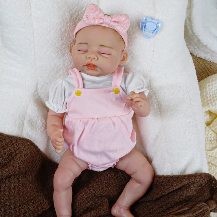 Adorable silicone reborn doll with a pink bow headband and a blue pacifier, dressed in a pink jumpsuit, giving the impression of a serene sleep.