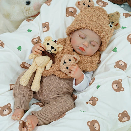 Reborn baby doll sleeping with a teddy bear on a bear-patterned blanket.