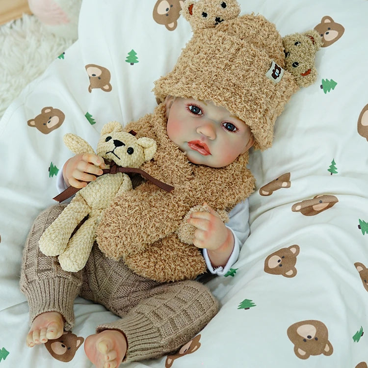 Reborn baby doll wearing a bear hat, holding a teddy bear.