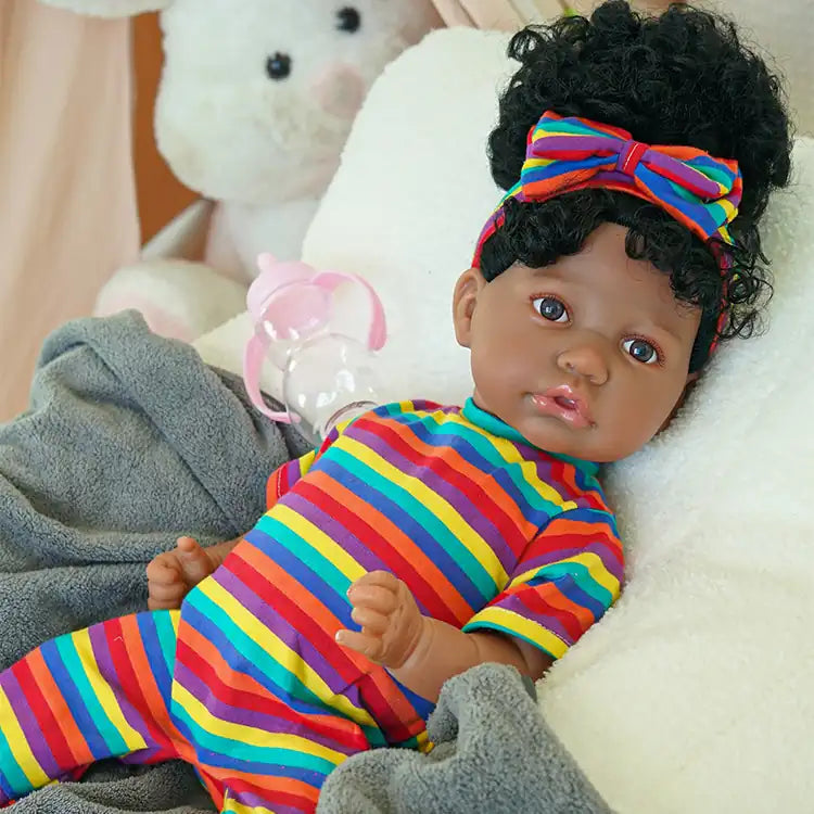 A black reborn baby doll lying on the sofa wearing multi-colored striped clothes
