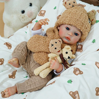 Reborn baby doll lying on a bear-themed blanket, holding a soft teddy bear.