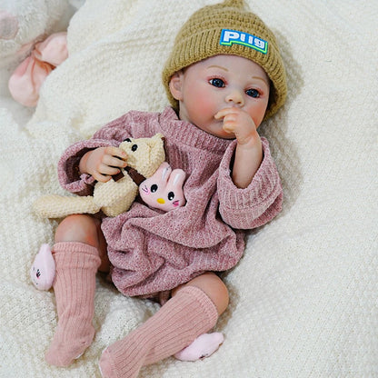 Reborn baby doll in a pink outfit, holding a teddy bear and rabbit toy.