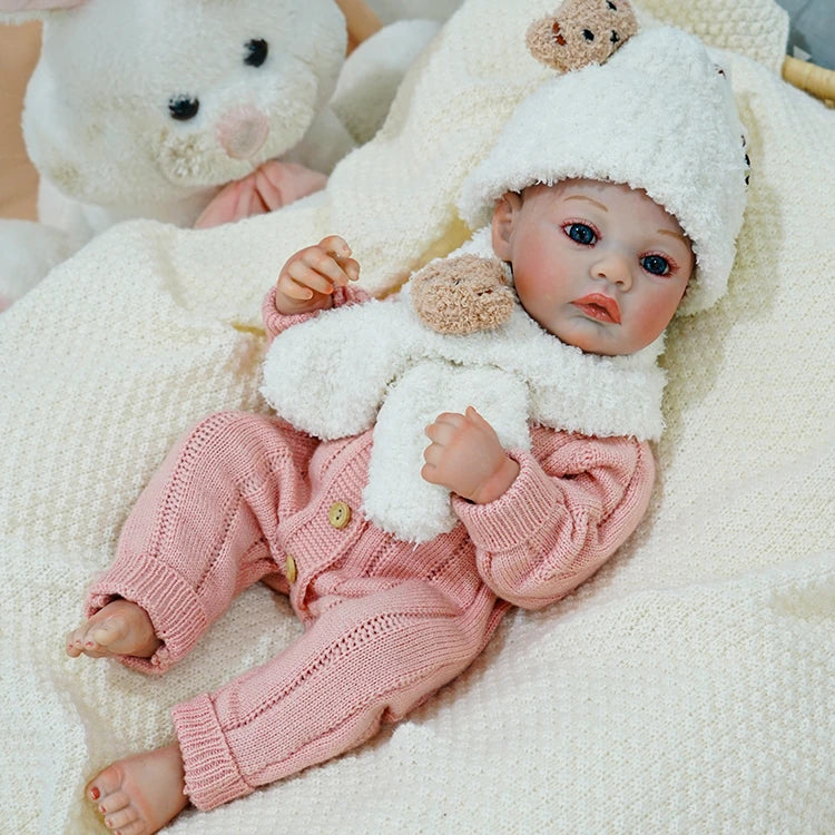 Reborn baby doll dressed in pink, resting peacefully with a teddy bear.