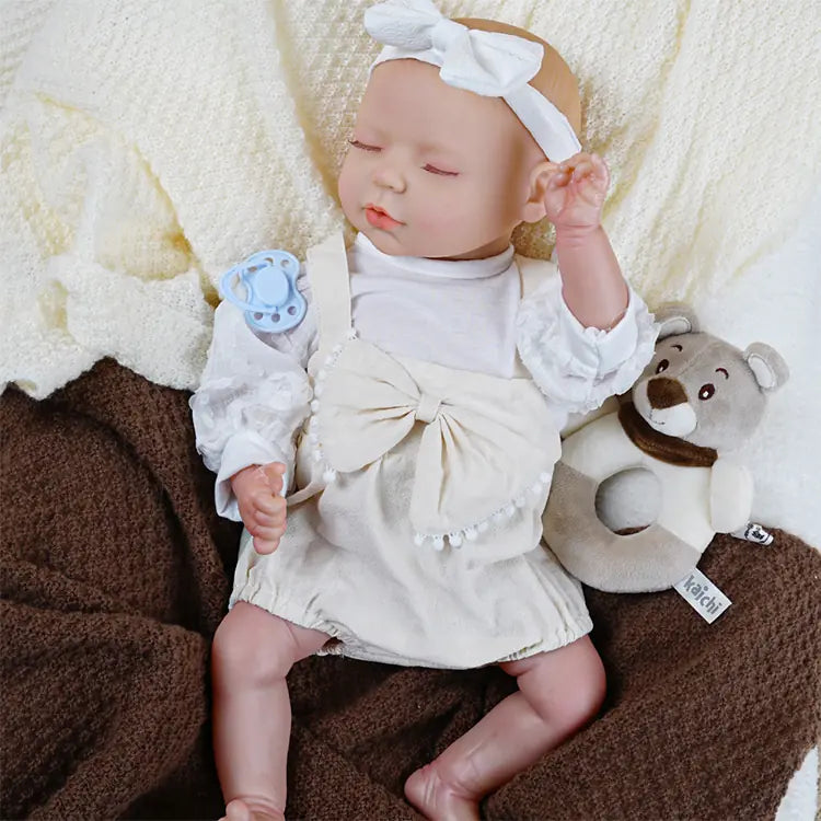 Newborn reborn doll in cream dress with bow details.