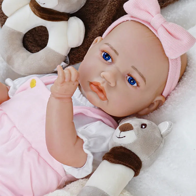Newborn doll replica in pink outfit with bear.