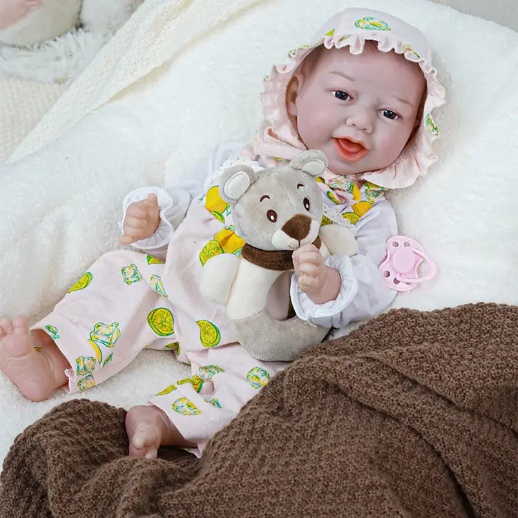 A cute reborn baby doll lying on the sofa holding a teddy bear doll