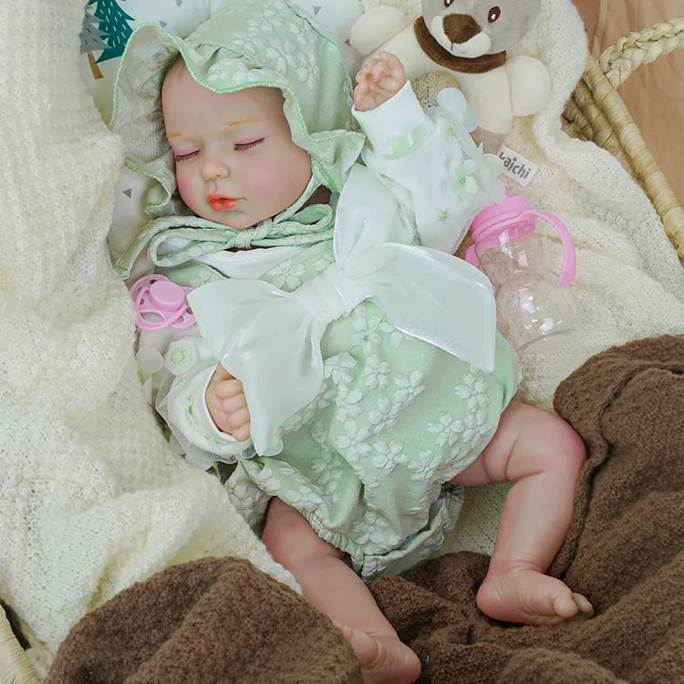 A serene reborn baby doll wrapped in a pale green floral romper and matching hood, peacefully sleeping in a wicker basket, nestled in a white knitted blanket, with a plush teddy bear and a pink bottle nearby.