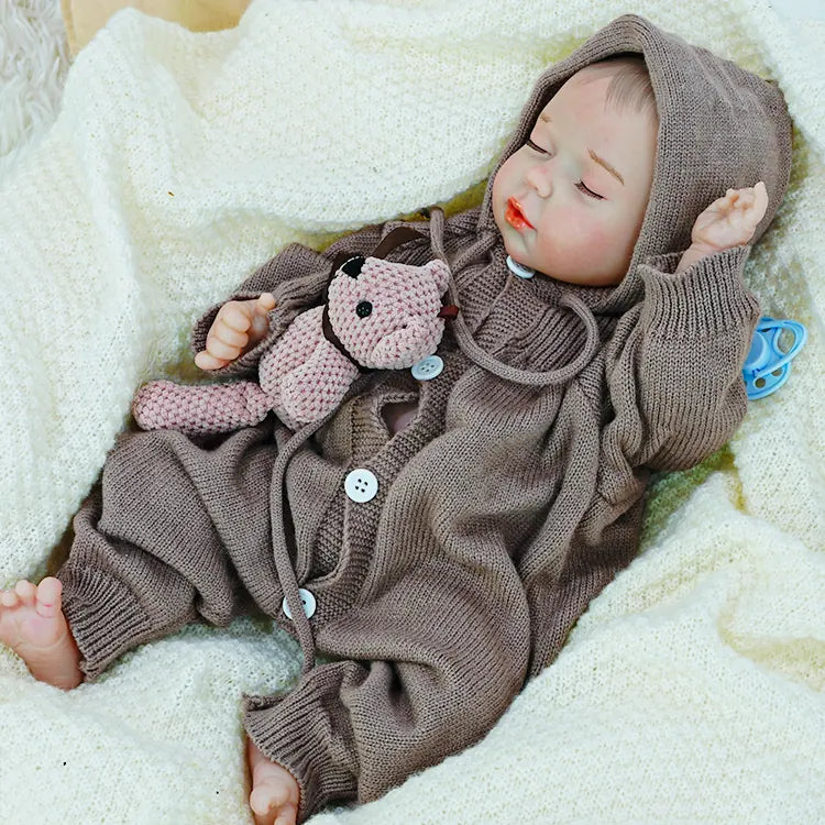  A reborn baby doll lying on its back, eyes closed, holding a teddy bear.