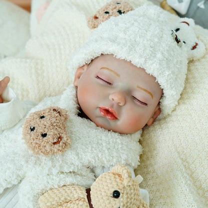 Reborn baby doll sleeping with a small teddy bear by its side.