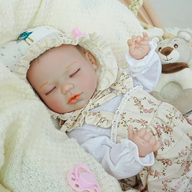 Close-up of a sleeping reborn baby doll wearing a floral bonnet, pink pacifier in mouth, nestled comfortably in a basket surrounded by a plush bear and soft white blanket.