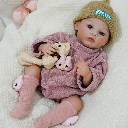 Reborn baby doll lying on a blanket, wearing a beanie and pink outfit.