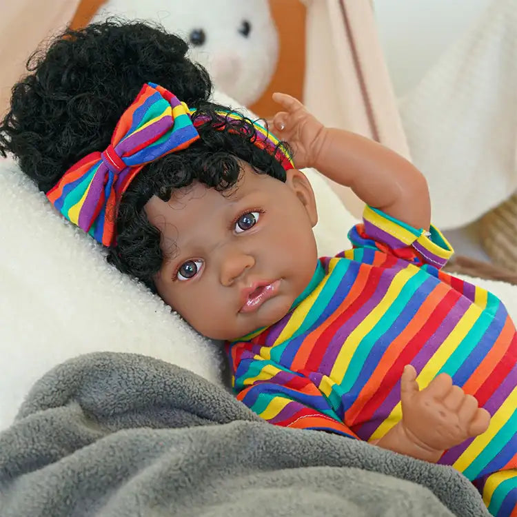A black reborn baby doll lying on the sofa wearing multi-colored striped clothes